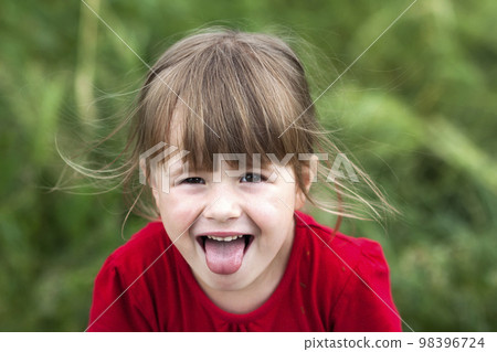 Smiling little girl shows tongue. Young cute little girl gesturing with her mouth. Smiling little girl shows tongue. Young cute little girl gesturing with her mouth. 98396724