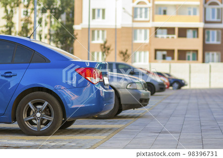Side view detail of cars row parked in paved yard parking lot area on blurred building background on bright sunny day. Transportation and parking concept. 98396731