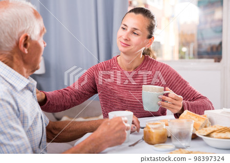 Elderly father and adult daughter talk and drink tea in the kitchen Elderly father and adult daughter talk and drink tea in the kitchen 98397324