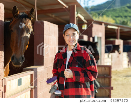 Portrait of young woman with brushes in her hands for cleaning and caring for horses at horse farm 98397370