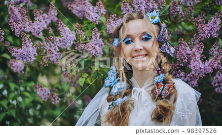A young girl poses in lilac with a beautiful hairstyle of flowers and butterflies. 98397526