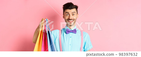 Image of happy guy on shopping, holding paper bags and smiling excited, shopper buying with discounts, standing on pink background Image of happy guy on shopping, holding paper bags and smiling excited, shopper buying with discounts, standing on pink background 98397632