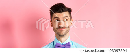 Close-up of handsome smiling guy with moustache, looking left at logo with pleased face, standing on pink background 98397894