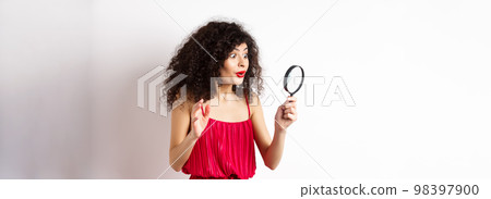 Excited woman in red dress look through magnifying glass and smiling, found interesting promo, standing on white background Excited woman in red dress look through magnifying glass and smiling, found interesting promo, standing on white background 98397900