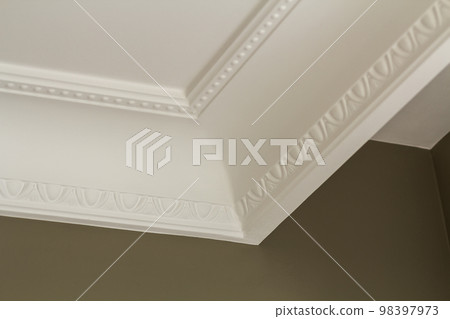 Ornamental white molding decor on ceiling of white room close-up detail. Interior renovation and construction concept. 98397973