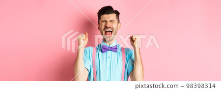 Relieved man shouting from happiness and joy, scream yes with closed eyes and clenched fists, celebrating victory, achieve goal and triumphing, standing over pink background Relieved man shouting from happiness and joy, scream yes with closed eyes and clenched fists, celebrating victory, achieve goal and triumphing, standing over pink background 98398314