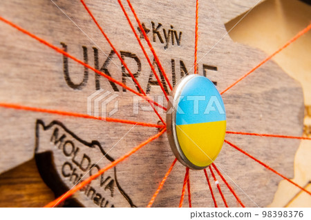 Ukraine flag on the pushpin with red thread showed the paths of movement or areas of influence in the global economy on the wooden map. Planning of traveling or logistic concept. Network connection.  98398376
