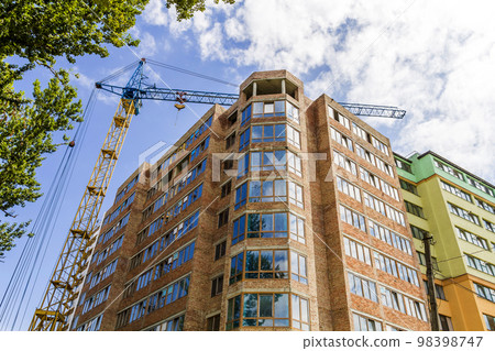 Modern high storey building under construction with tower crane and green tree 98398747