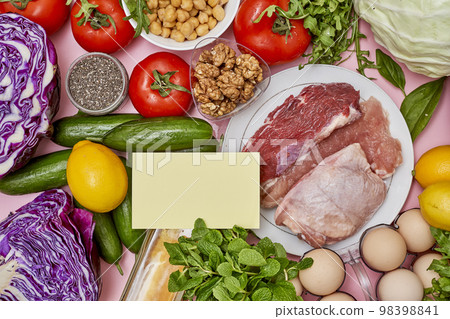 some food that is on a pink surface with vegetables, eggs, lemons, tomatoes, and other foods 98398841