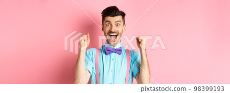 Happy guy winning prize, screaming with joy yes, shaking hands and celebrating victory, achieve success and triumphing over pink background 98399193