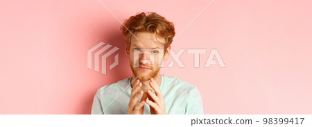 Close up of funny bearded man with red hair pitching a perfect plan, smiling and steeple fingers, scheming something, standing devious against pink background 98399417