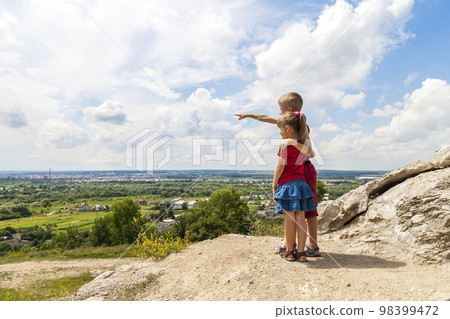 Little children boy and girl standing on mountain rock and looking ahead. Boy showing with his hand Little children boy and girl standing on mountain rock and looking ahead. Boy showing with his hand 98399472