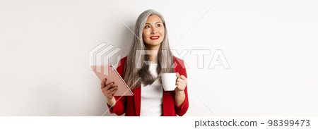 Business people concept. Asian businesswoman drinking coffee and holding digital tablet, smiling thoughtful at upper left corner, white background Business people concept. Asian businesswoman drinking coffee and holding digital tablet, smiling thoughtful at upper left corner, white background 98399473