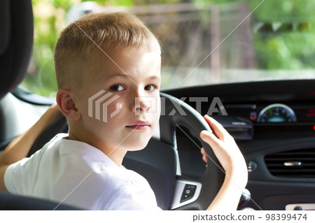 Little child boy behind the steering wheel of a car Little child boy behind the steering wheel of a car 98399474