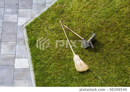 Jug dustpan and a broom on a green grass lawn. Gardening tools. 98399540