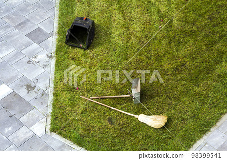 Jug dustpan and a broom on a green grass lawn. Gardening tools. 98399541