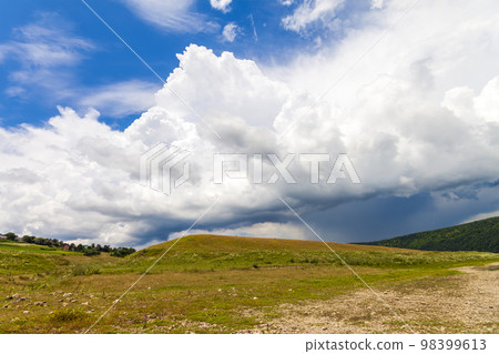 Hill with green grass and dramatic storm clouds overhead Hill with green grass and dramatic storm clouds overhead 98399613