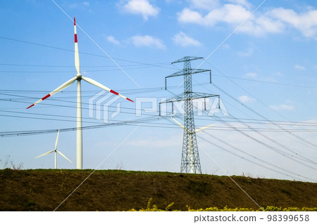 High voltage tower and wind turbines against blue sky 98399658