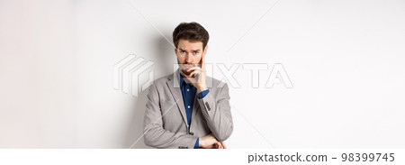 Troubled frowning business man in suit looking at camera pensive, thinking or making decision, standing on white background 98399745