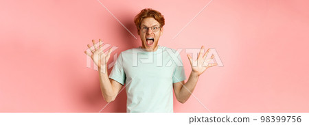Angry and pressured young man losing temper, spread hands sideways and screaming with furious face, standing in glasses and t-shirt against pink background 98399756