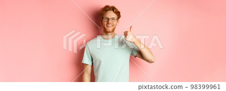 Cheerful redhead man in glasses and t-shirt, showing thumbs up with satisfied face, showing positive reaction, approve and agree with you, standing over pink background Cheerful redhead man in glasses and t-shirt, showing thumbs up with satisfied face, showing positive reaction, approve and agree with you, standing over pink background 98399961