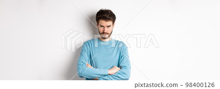 Image of offended and sad young man with beard, look from under forehead and sulking irritated, cross arms on chest defensive, mad at someone, standing on white background 98400126