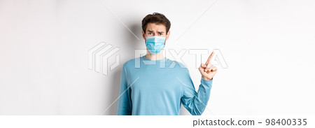 Coronavirus, health and quarantine concept. Skeptical man in medical mask pointing finger left at logo, frowning disappointed, standing over white background Coronavirus, health and quarantine concept. Skeptical man in medical mask pointing finger left at logo, frowning disappointed, standing over white background 98400335