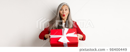 Surprised asian senior woman receiving present on mother day, holding red box with gift and looking amazed at camera, white background 98400449