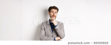 Thoughtful businessman in suit touching beard, thinking and looking at camera, deciding with pensive face, standing on white background Thoughtful businessman in suit touching beard, thinking and looking at camera, deciding with pensive face, standing on white background 98400608