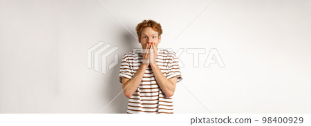 Surprised and excited man with curly red hair checking out special promo offer,staring fascinated and amazed, covering mouth with hands, standing over white background Surprised and excited man with curly red hair checking out special promo offer,staring fascinated and amazed, covering mouth with hands, standing over white background 98400929