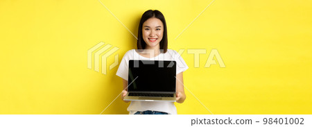 Young asian woman demonstrate online offer, showing laptop screen and smiling, standing over yellow background Young asian woman demonstrate online offer, showing laptop screen and smiling, standing over yellow background 98401002