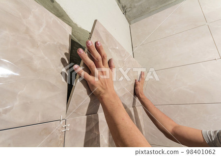 Close-up of worker tiler hands installing light beige ceramic tiles on walls of future bathroom. Tiles installation, home improvement, renovation and construction, comfortable modern home concept. Close-up of worker tiler hands installing light beige ceramic tiles on walls of future bathroom. Tiles installation, home improvement, renovation and construction, comfortable modern home concept. 98401062