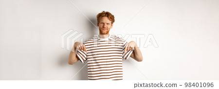Disappointed redhead man shaking head displeased, showing something bad, pointing fingers down with skepical face, white background 98401096