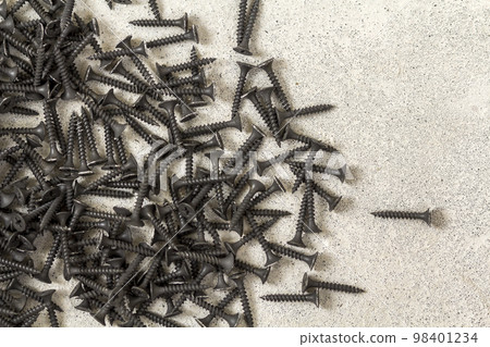 Close-up image of many small black screws on concrete background 98401234