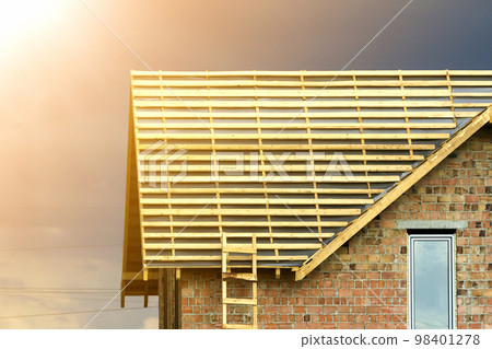 Close-up detail of new brick house top with two narrow plastic attic windows and wooden roof frame under construction on dark blue sky background. Real estate property and professional work concept. 98401278
