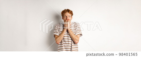 Shocked redhead guy gossiping, giggle in hands and looking left impressed, standing over white background 98401565
