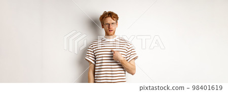 Confused redhead man in glasses pointing at himself, looking questioned at camera, white background Confused redhead man in glasses pointing at himself, looking questioned at camera, white background 98401619