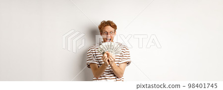 Lucky young man with red hair showing dollars, winning money and screaming of happiness, holding prize cash, standing over white background Lucky young man with red hair showing dollars, winning money and screaming of happiness, holding prize cash, standing over white background 98401745