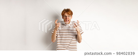 Portrait of redhead male student looking annoyed and pissed-off, shaking hands and staring angry at camera, shouting at someone, standing over white background 98402839