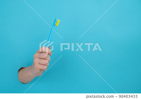 A woman's hand sticks out of a blue paper background and holds a toothbrush.  98403433