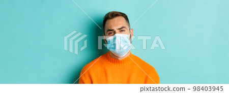 Covid-19, social distancing and quarantine concept. Upset man in face mask complaining, looking displeased and tired, standing against light blue background Covid-19, social distancing and quarantine concept. Upset man in face mask complaining, looking displeased and tired, standing against light blue background 98403945