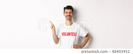 Handsome smiling volunteer in t-shirt pointing finger left, showing announcement, standing over white background 98403952