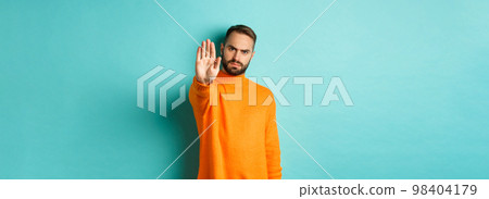 Serious frowning man showing stop gesture, telling no, prohibit and disagree, standing over light blue background Serious frowning man showing stop gesture, telling no, prohibit and disagree, standing over light blue background 98404179
