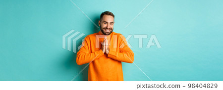 Happy man saying thank you, holding hands in pray, looking grateful and smiling, standing over light blue background 98404829