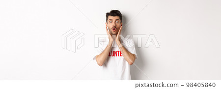Shocked man in volunteer t-shirt gasping, staring at camera in awe, standing over white background 98405840
