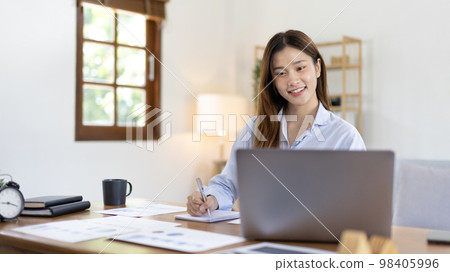 Beautiful young asian woman watching live video or video call of teacher teaching on laptop in her home, Take notes of important conversations and messages during the teacher's teaching. Beautiful young asian woman watching live video or video call of teacher teaching on laptop in her home, Take notes of important conversations and messages during the teacher's teaching. 98405996