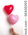 Inflatable helium balloons in the shape of a heart for Valentine's Day are held by a girl in her hand. Front view. 98406005