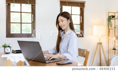 Beautiful young asian woman watching live video or video call of teacher teaching on laptop in her home, Take notes of important conversations and messages during the teacher's teaching. 98406153