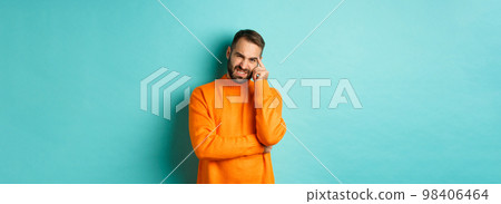 Man with beard, grimacing and cringe from something embarrassing, looking with awkward face, standing over light blue background 98406464