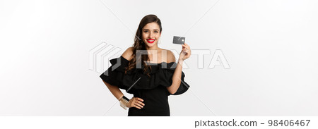 Beauty and shopping concept. Stylish pretty woman with red lips, black dress, smiling happy and showing credit card, standing over white background Beauty and shopping concept. Stylish pretty woman with red lips, black dress, smiling happy and showing credit card, standing over white background 98406467